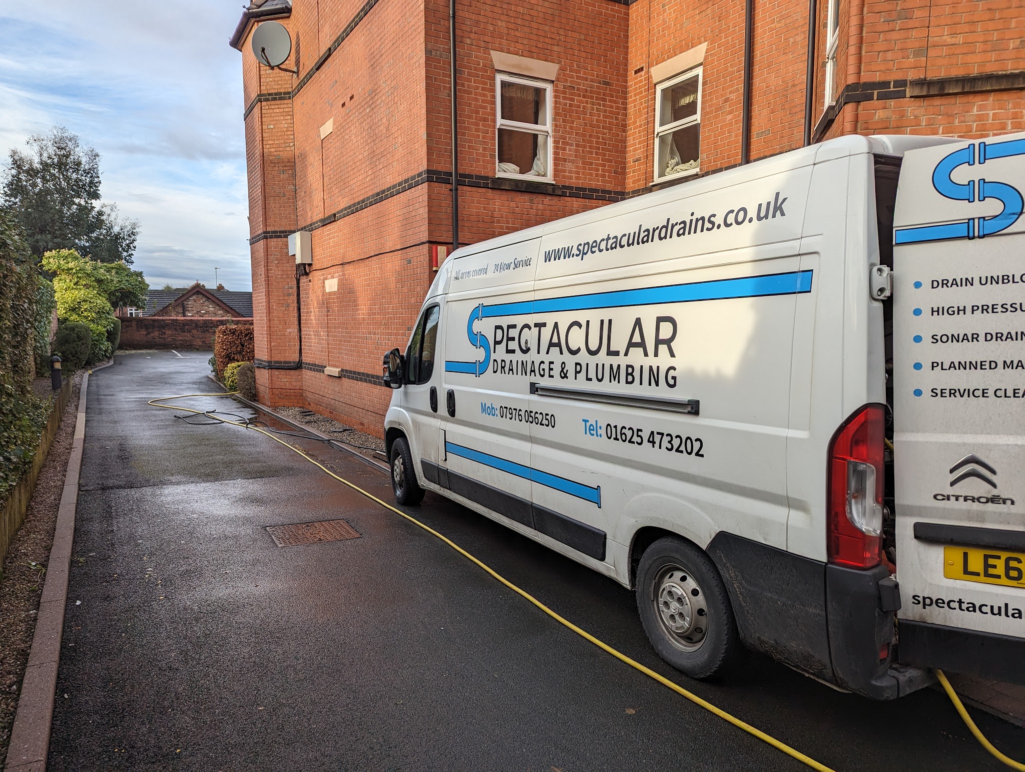 The Spectacular Drainage & Plumbing van parked beside a brick building with a jetting hose laid out down the lane
