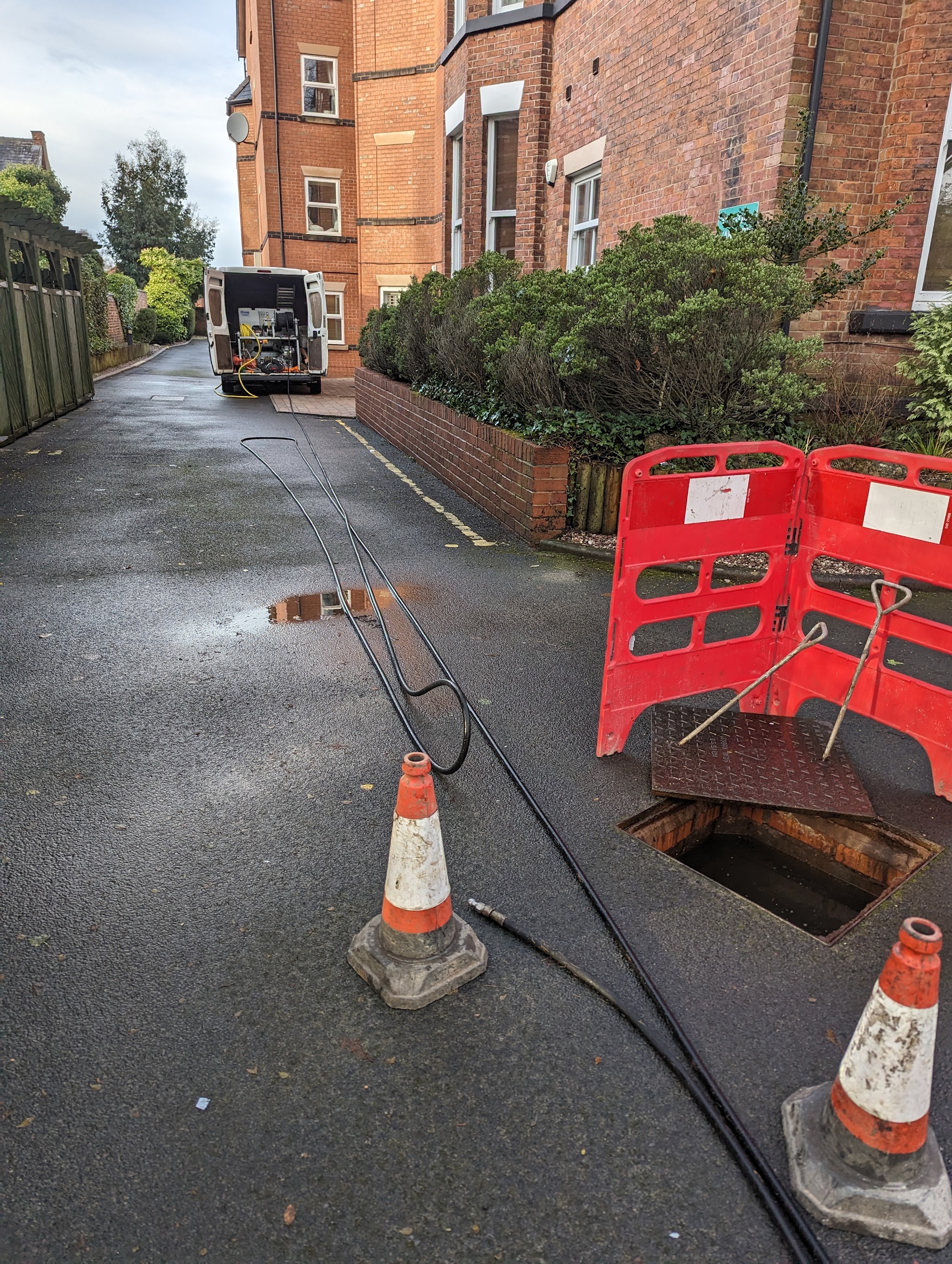A drain chamber with a red barrier and jetting lines running back to the van